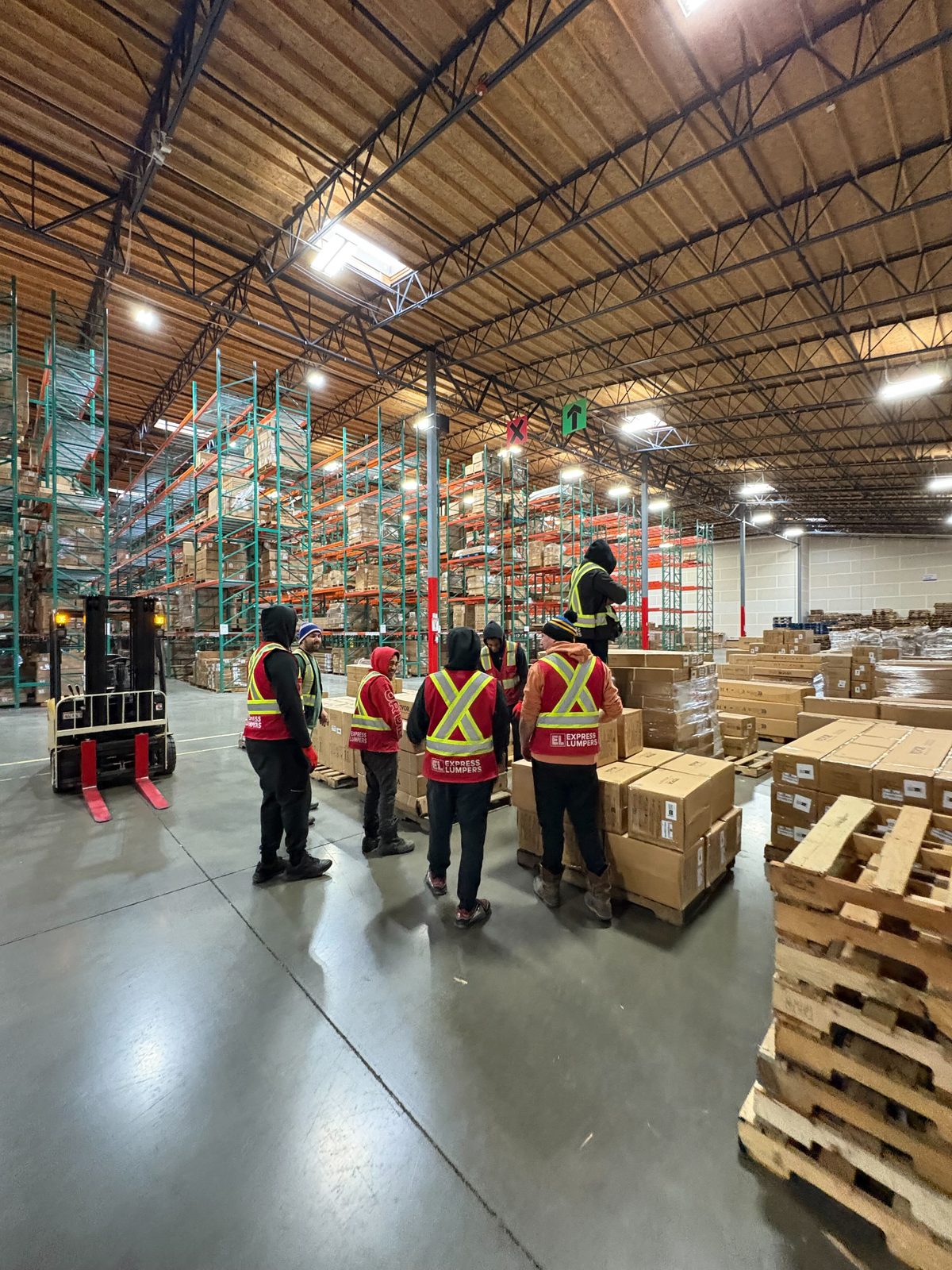 Express Lumpers crew briefing around palletized freight in a Renton warehouse